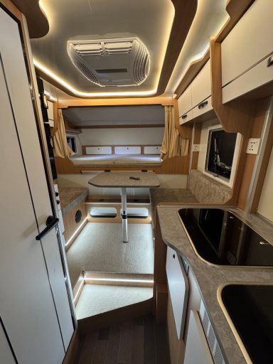 Helle, moderne Wohnmobilküche mit Platz für Tisch, Stühlen, Kochfeld und Schränken.