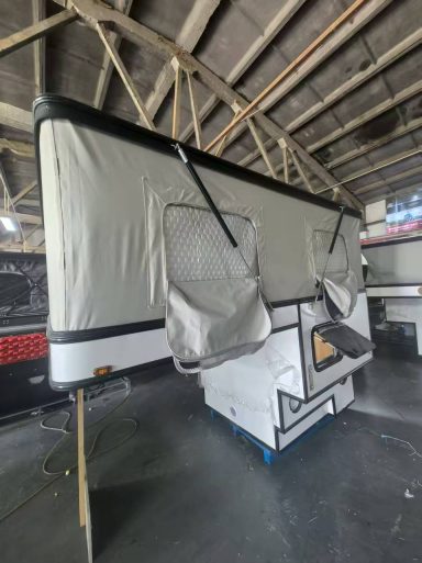 Ein aufgeklappter Campinganhänger mit grauer Abdeckung in einer Halle.