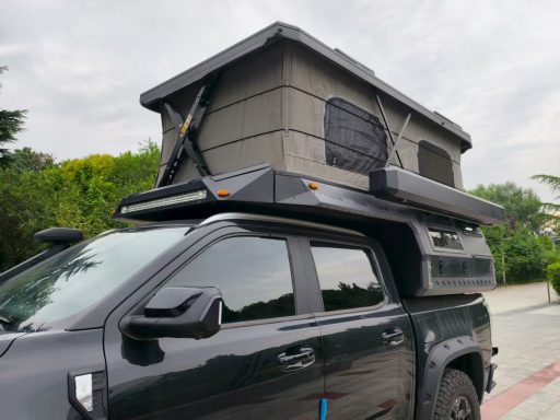 Schwarzer Pickup mit Dachzelt auf dem Fahrzeugdach, in einer grünen Umgebung.