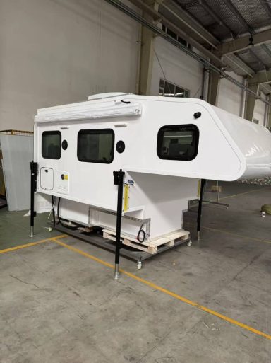 Weißes Camper-Modul mit mehreren Fenstern, auf Stützen stehend in einer Halle.