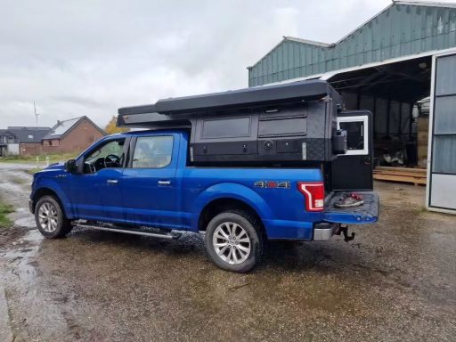 Blaues Pickup-Fahrzeug mit einem schwarzen Aufstelldach in einer ländlichen Umgebung.