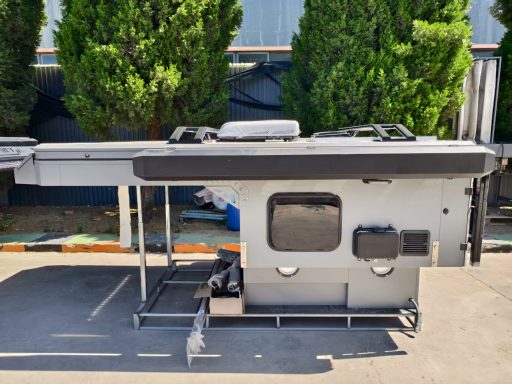 Ein grau-weißes Wohnmobil mit einem flachen Dach, seitlich mit Fenster und Stauraum.