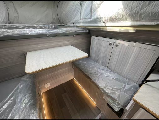 Heller Innenraum mit Tisch, Bank und Regalen, teilweise mit Folie abgedeckt.