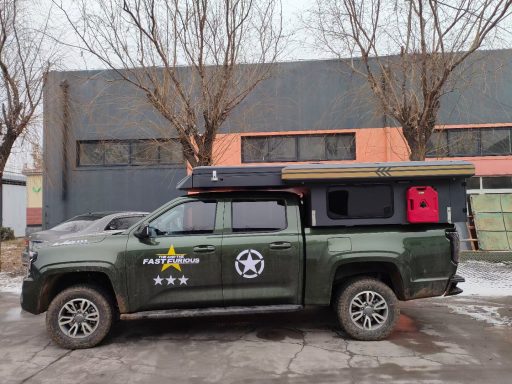 Ein grüner Pickup mit Dachzelt und rotem Gepäck, geparkt vor einem Gebäude.