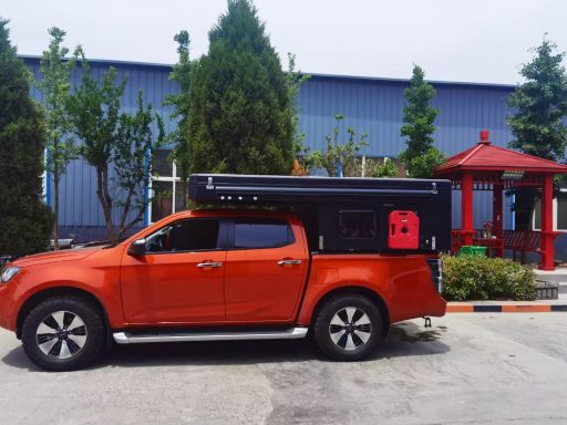 Leuchtend orange Pickup-Truck mit schwarzem Überbau, im Hintergrund grüne Bäume und ein Pavillon.