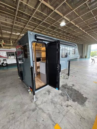 Kleiner Wohnanhänger mit offener Tür, moderne Inneneinrichtung, in einer Halle geparkt.