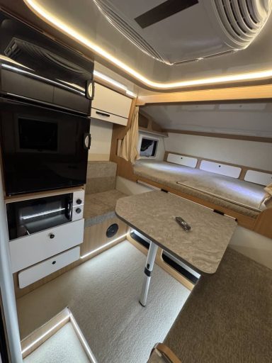 Moderne Wohnmobil-Inneneinrichtung mit Tisch, Küche und Schlafbereich.