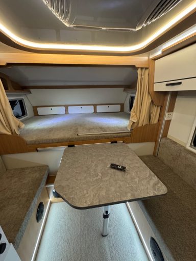 Kleine Wohnmobileinheit mit Sitzgruppe, Tisch und Hochbett im Hintergrund.