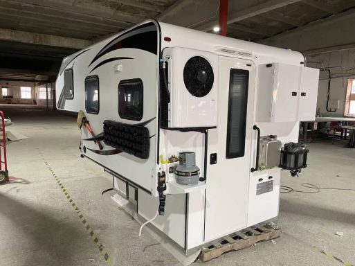 Ein weißer Wohnanhänger mit schwarzen und grauen Akzenten, in einem großen Innenraum.