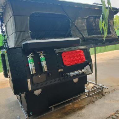 Schwarzes Wohnmobil mit klappbarem Dach und Feuerlöschern an der Seite.