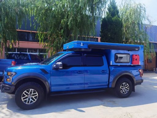 Blauer Pickup-Truck mit einem überdachten Aufsatz und Campingausrüstung auf der Ladefläche.